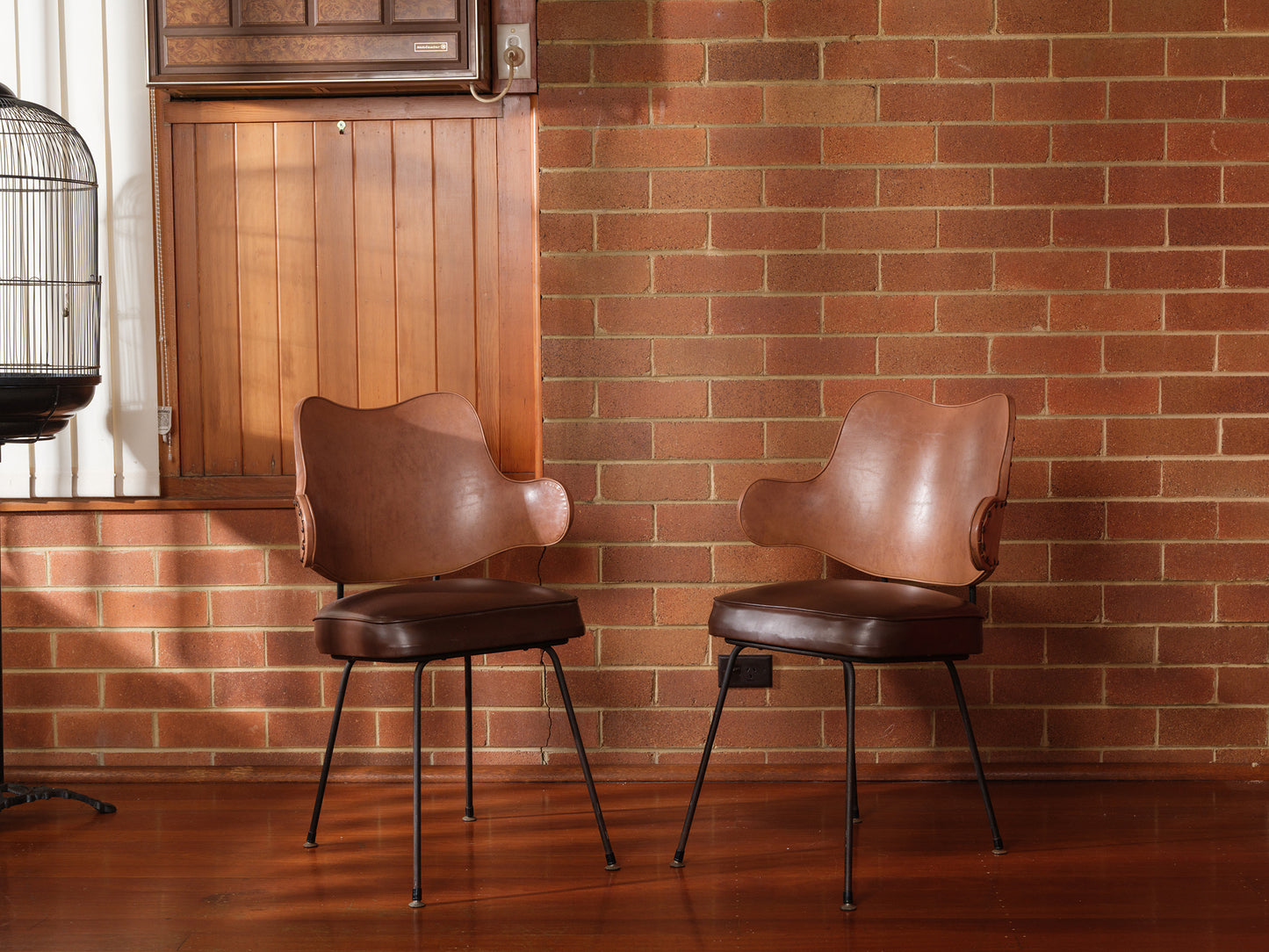 Two brown leather chairs against a brick wall with wooden paneling.