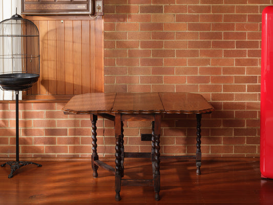 Antique oak gateleg dining table with barley twist legs, drop-leaf design against brick wall background