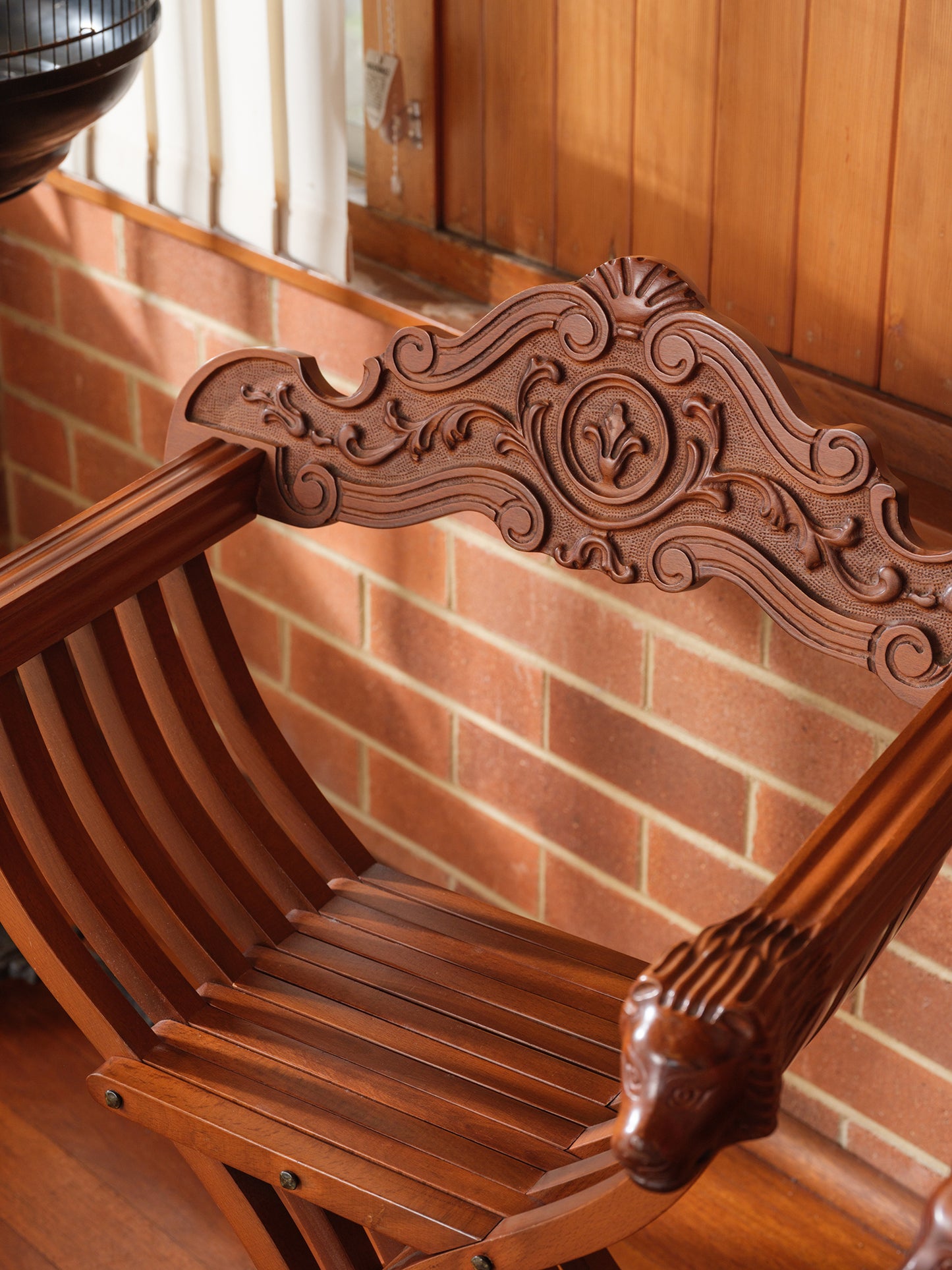 Antique wooden carved chair with lion head details in interior corner with birdcage background