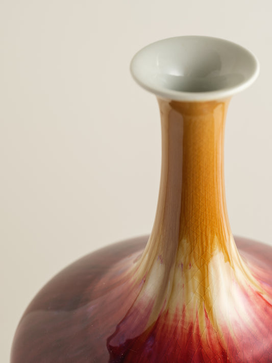 Flambé-glazed vase with a flared neck and rich gradient of crimson, amber, and deep oxblood hues.