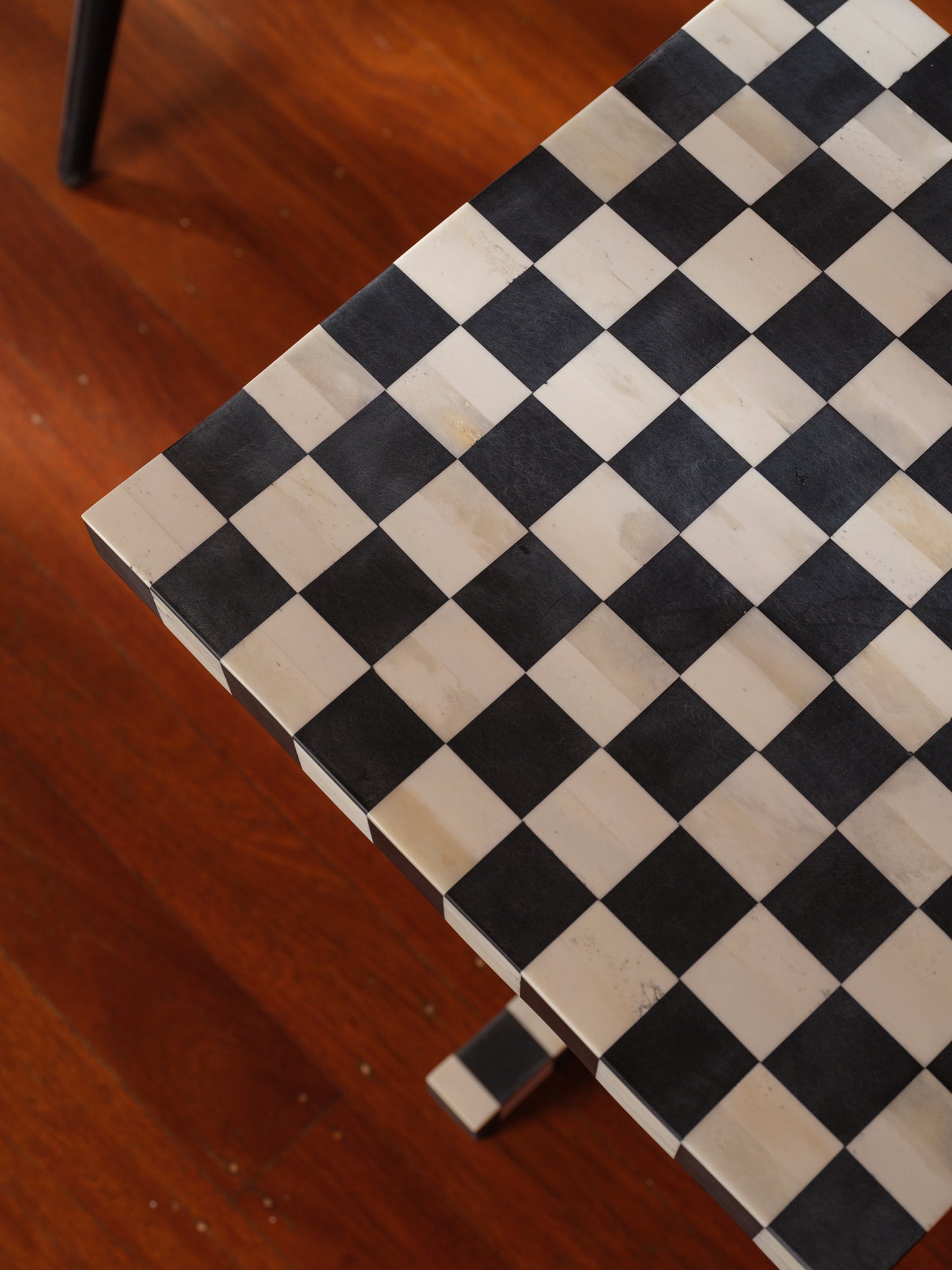 Modern black and white checkerboard side table with square top and pedestal base with brick wall background