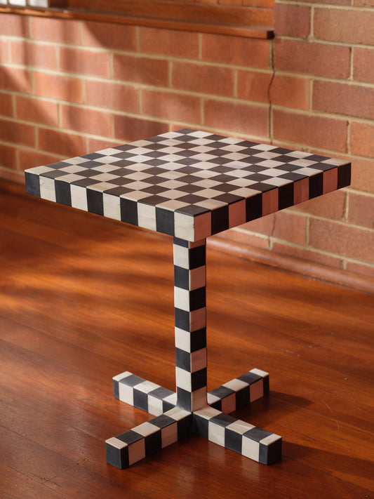 Modern black and white checkerboard side table with square top and pedestal base with brick wall background