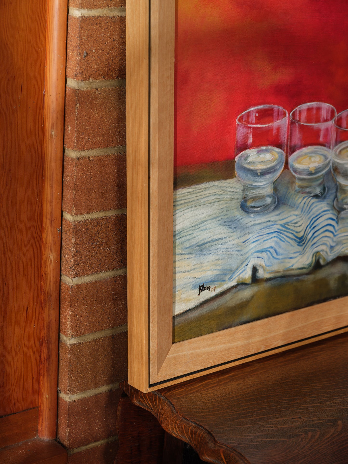 Oil painting titled Cobalt Pitcher and Glasses, featuring a deep blue jug and six clear glasses arranged on a striped cloth with a rich red background.