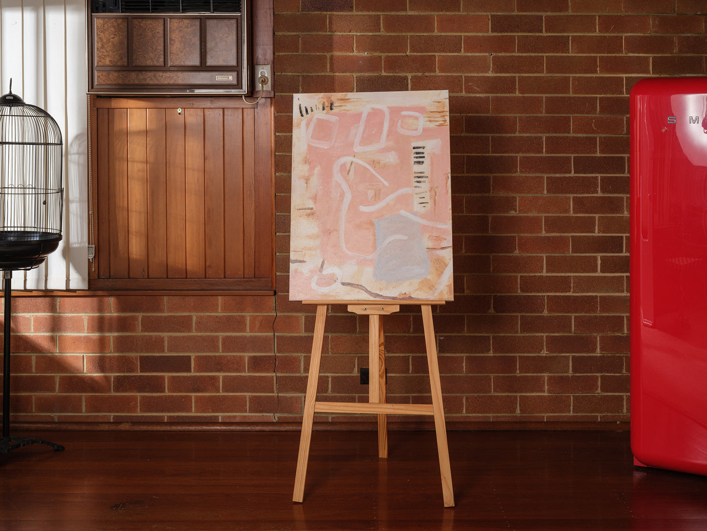 Abstract painting titled Drift in Pink, featuring soft pink and beige tones on canvas, displayed on wooden easel.
