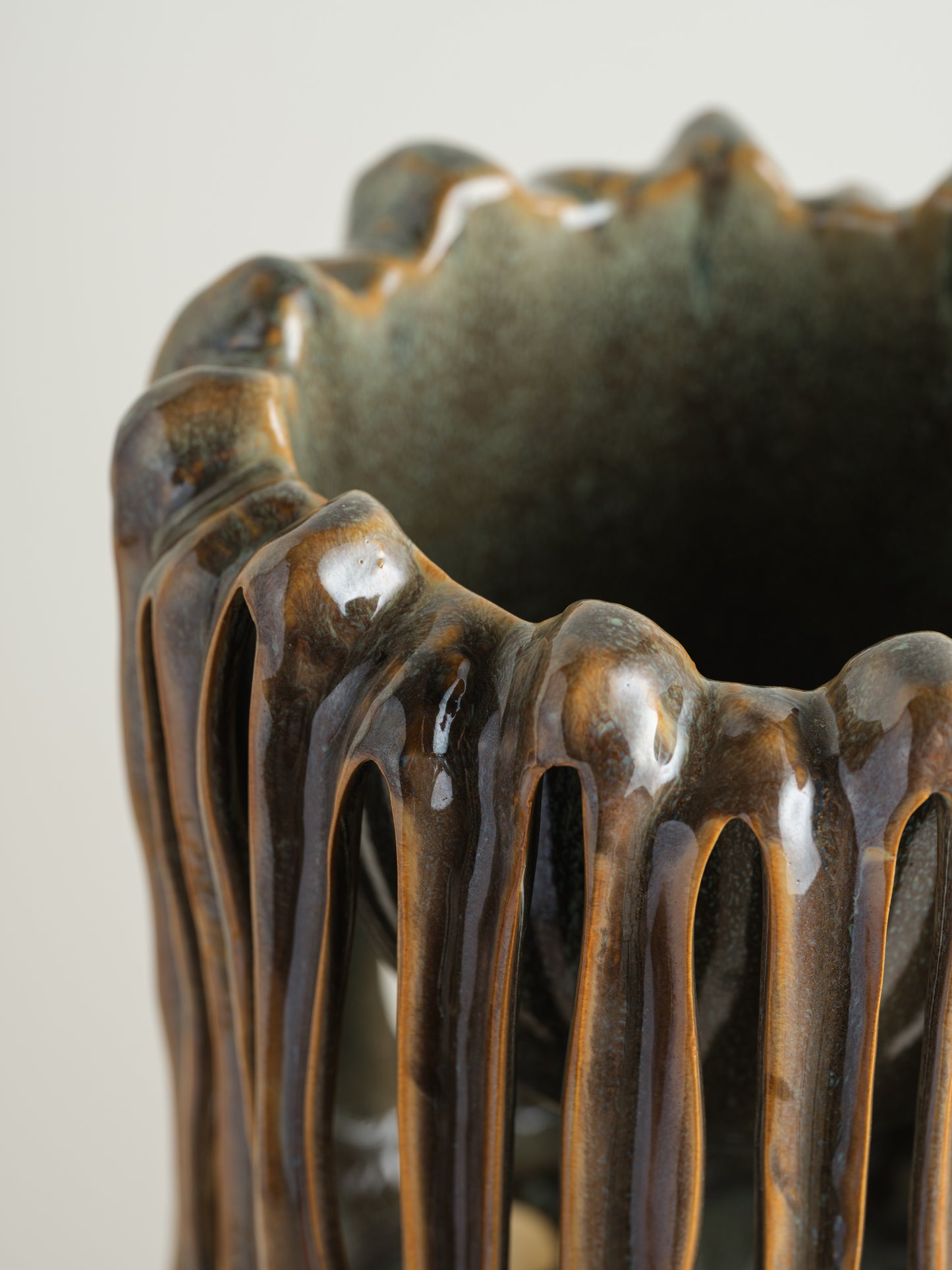 Ceramic vessel titled Drip Cage Vessel, featuring vertical dripping glaze lines forming an openwork cage-like structure with earthy brown and blue tones.