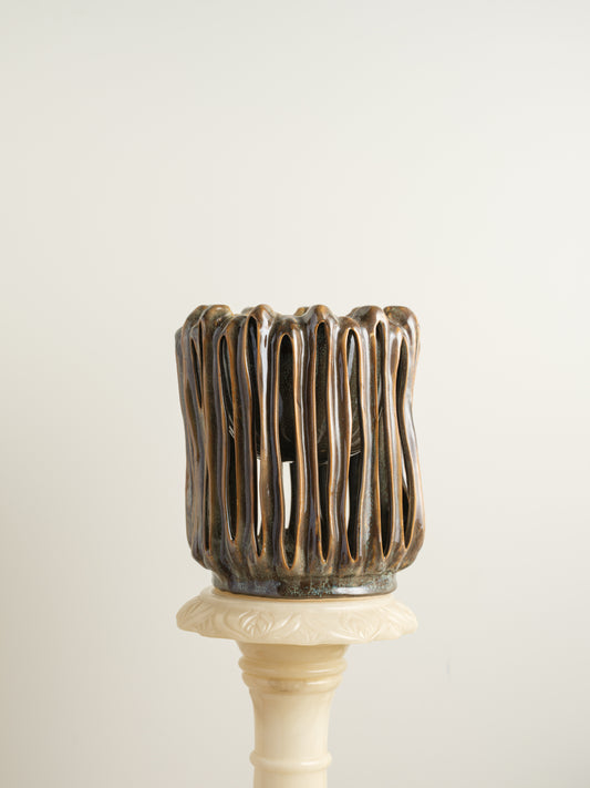Ceramic vessel titled Drip Cage Vessel, featuring vertical dripping glaze lines forming an openwork cage-like structure with earthy brown and blue tones.