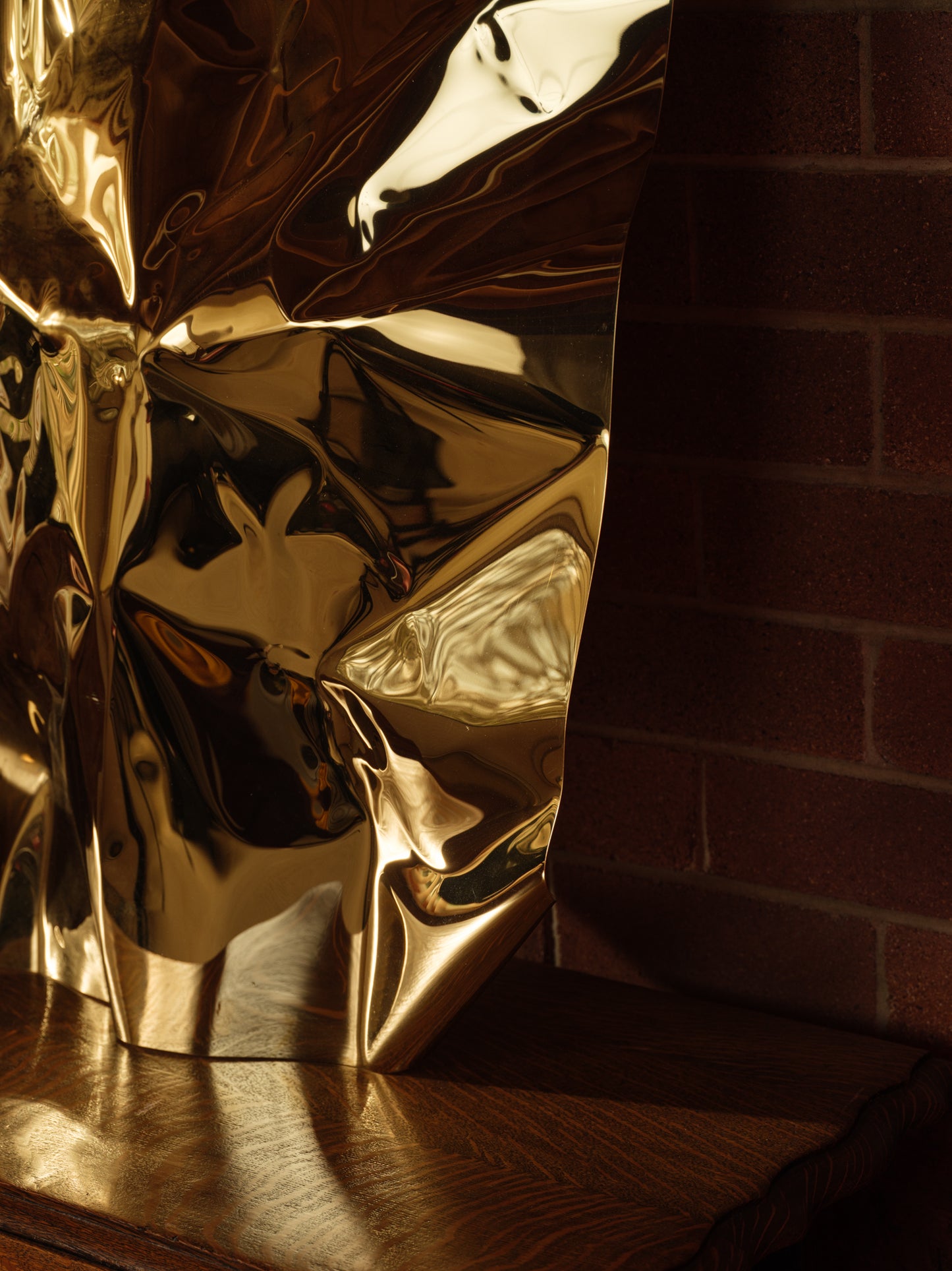 Sculpture titled Gilded Fold, made of polished stainless steel with a reflective golden surface and folded geometric form.