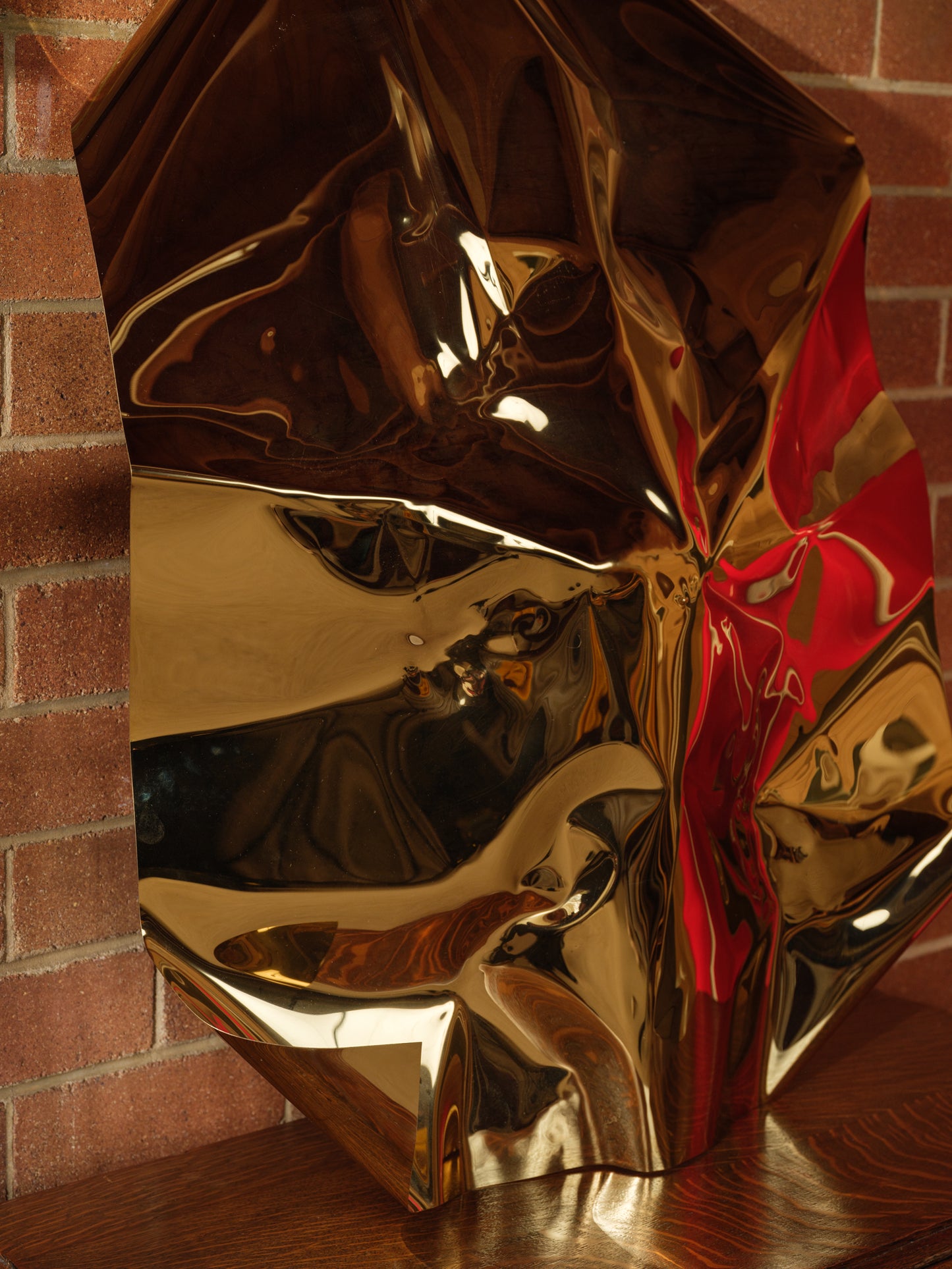 Sculpture titled Gilded Fold, made of polished stainless steel with a reflective golden surface and folded geometric form.