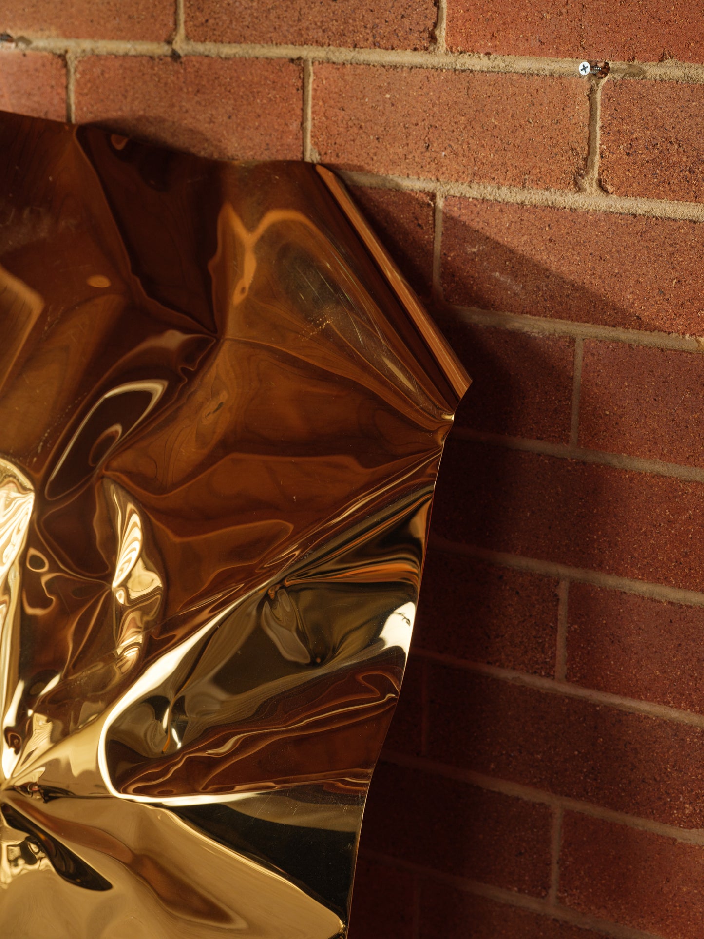 Sculpture titled Gilded Fold, made of polished stainless steel with a reflective golden surface and folded geometric form.