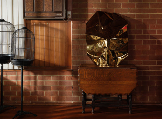 Sculpture titled Gilded Fold, made of polished stainless steel with a reflective golden surface and folded geometric form.