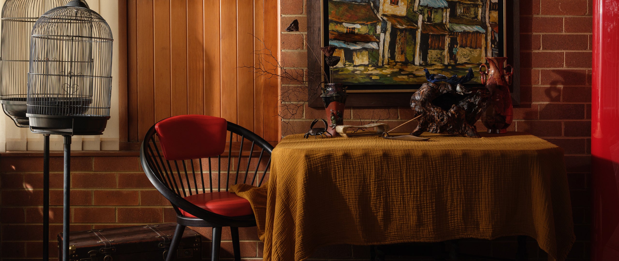 Hero banner featuring styled interior vignette with a red chair, vintage birdcages, rustic table setting with ceramic vases, and framed artwork, curated by SYP Homes.