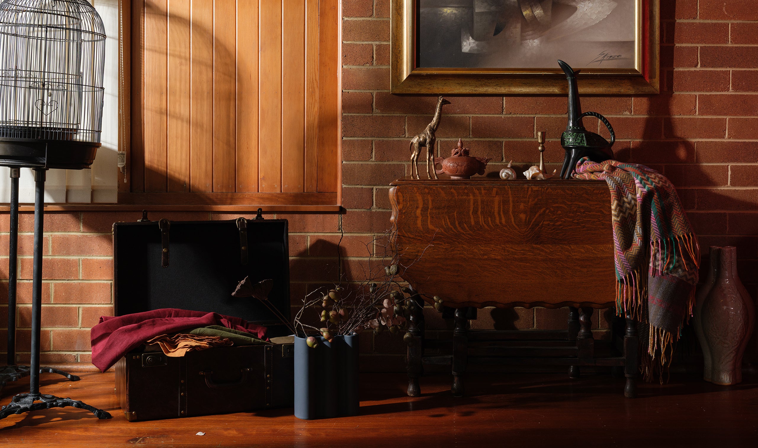 Image banner featuring a styled vignette with vintage suitcases, textiles, decorative giraffe figurine, ceramic vases, and eclectic objects on a wooden table, curated by SYP Homes.