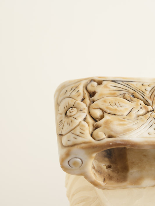 Ivory-toned pedestal stand with curved top and carved detailing, ideal for displaying vases or sculptures.