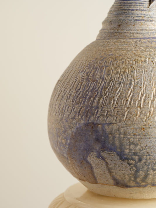 Hand-thrown stoneware ewer with lavender and sand-toned glaze and textured surface.