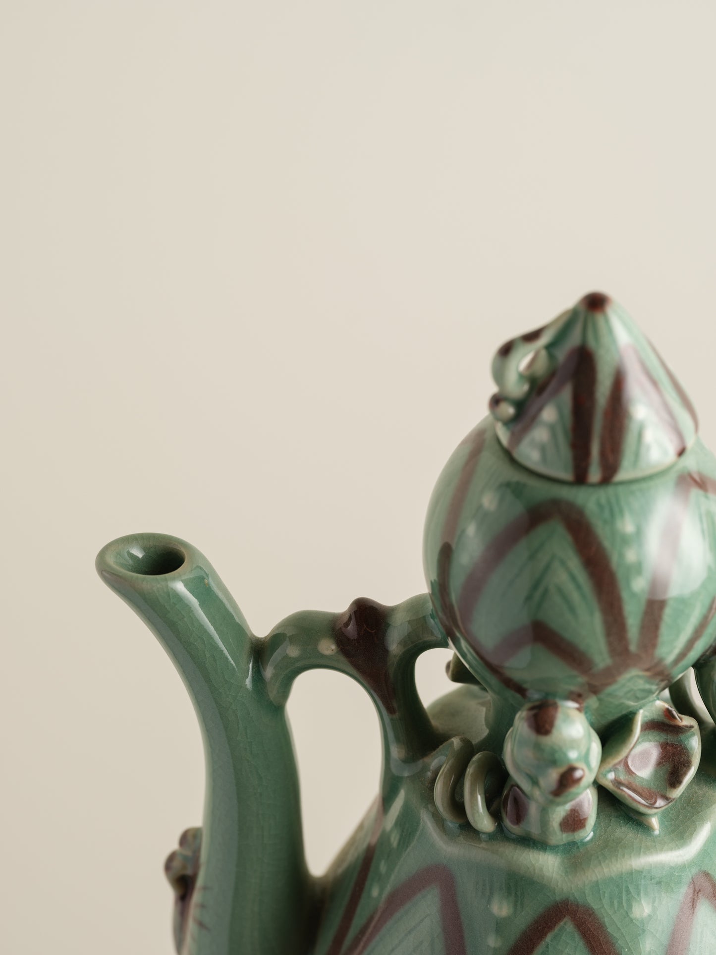 Celadon ewer with lotus petal relief design and sculpted handle and spout, finished in green glaze with brown accents.