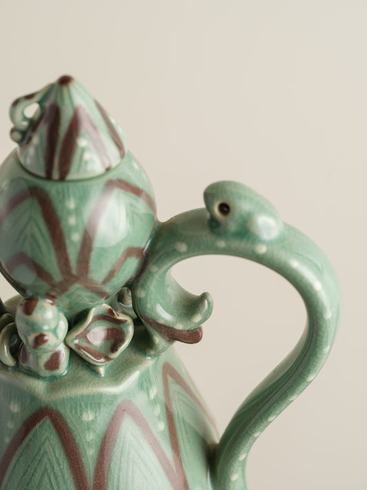 Celadon ewer with lotus petal relief design and sculpted handle and spout, finished in green glaze with brown accents.