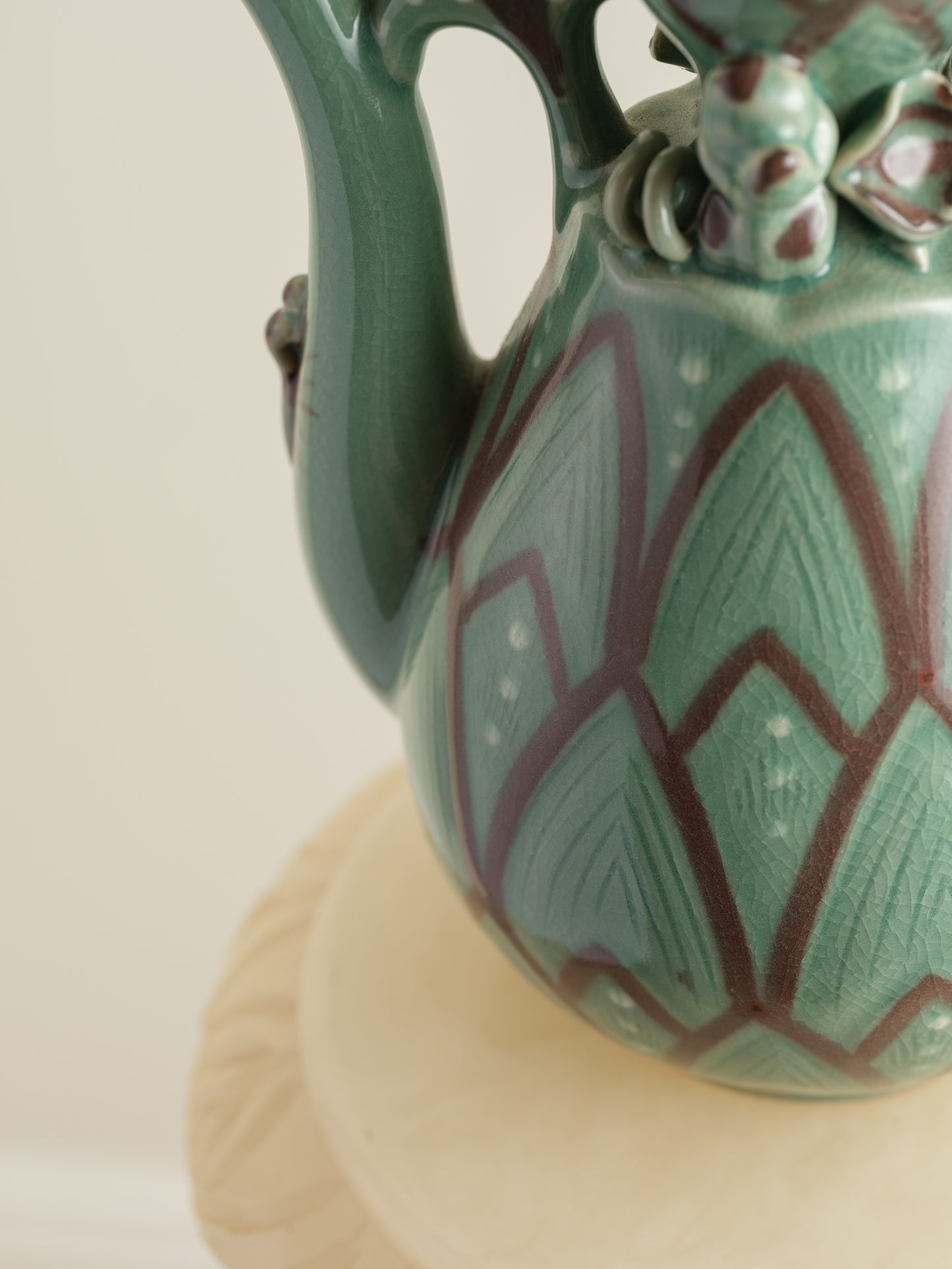 Celadon ewer with lotus petal relief design and sculpted handle and spout, finished in green glaze with brown accents.