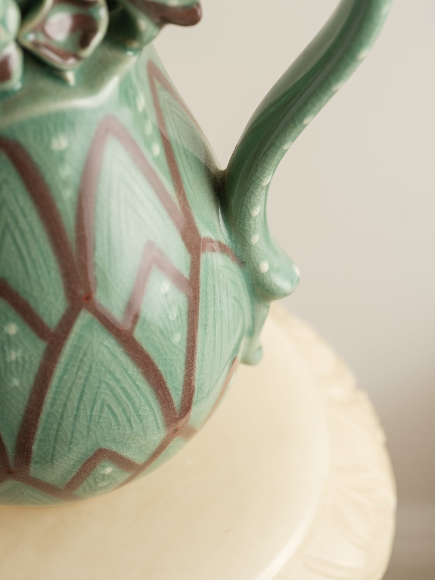 Celadon ewer with lotus petal relief design and sculpted handle and spout, finished in green glaze with brown accents.