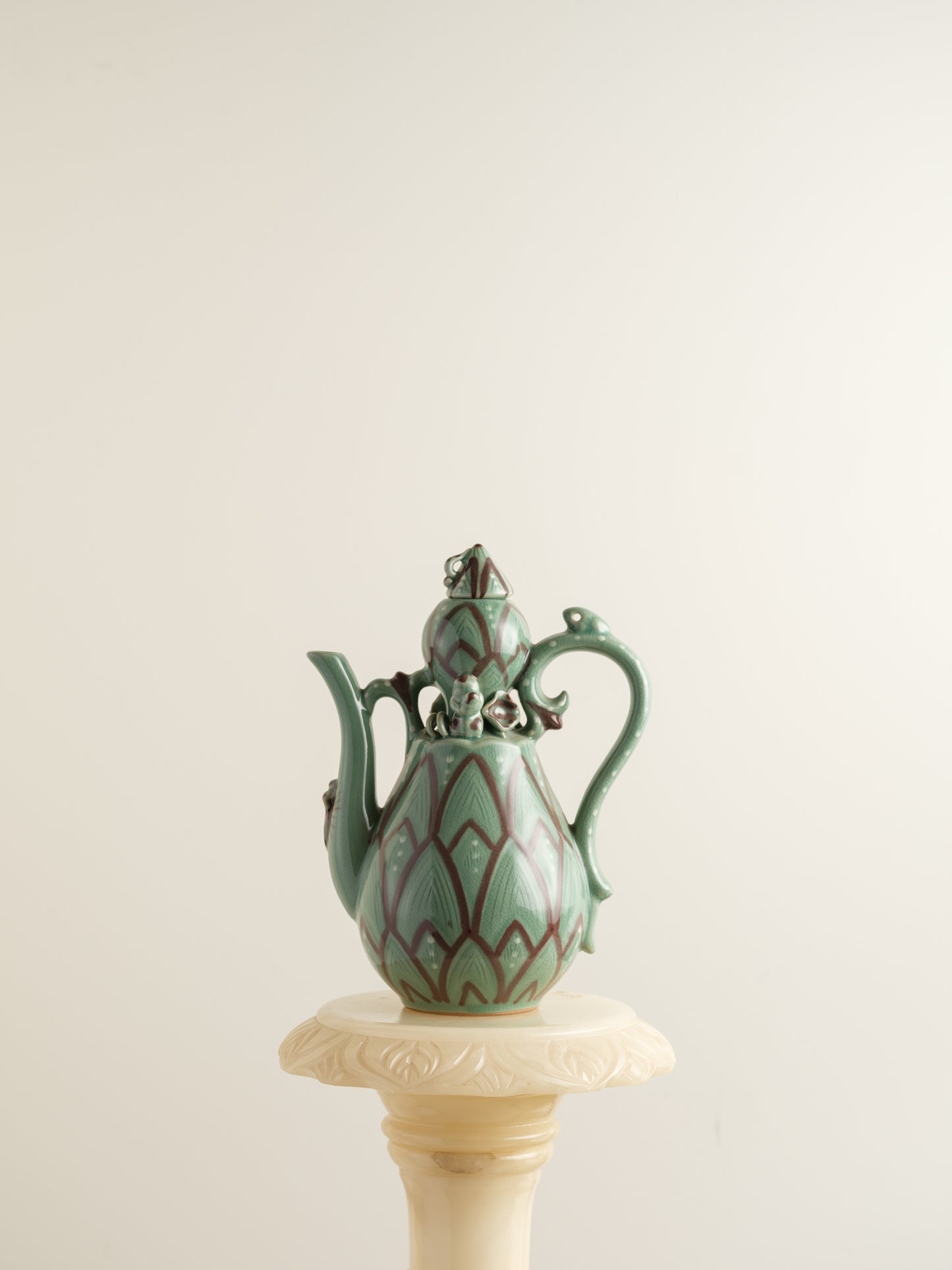 Celadon ewer with lotus petal relief design and sculpted handle and spout, finished in green glaze with brown accents.