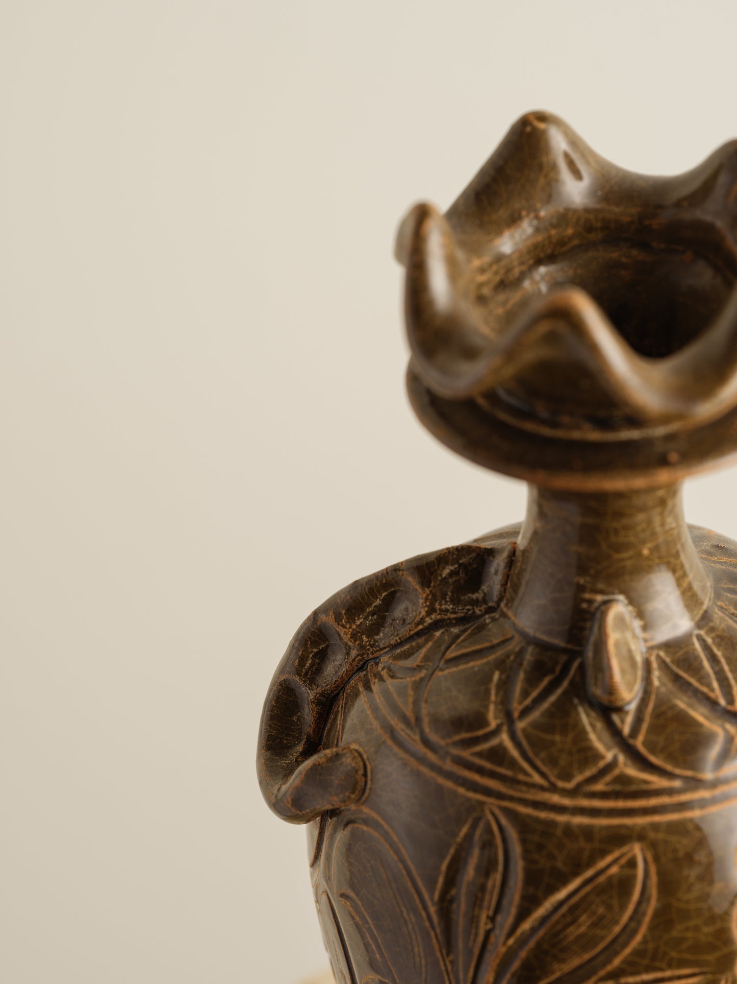 Brown stoneware ewer with carved lotus motif and flared crown-shaped mouth.