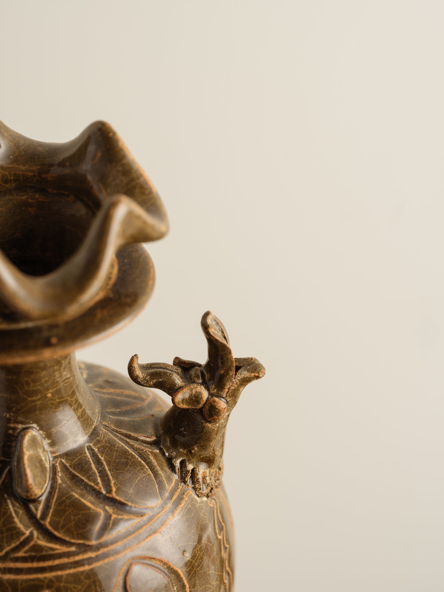 Brown stoneware ewer with carved lotus motif and flared crown-shaped mouth.
