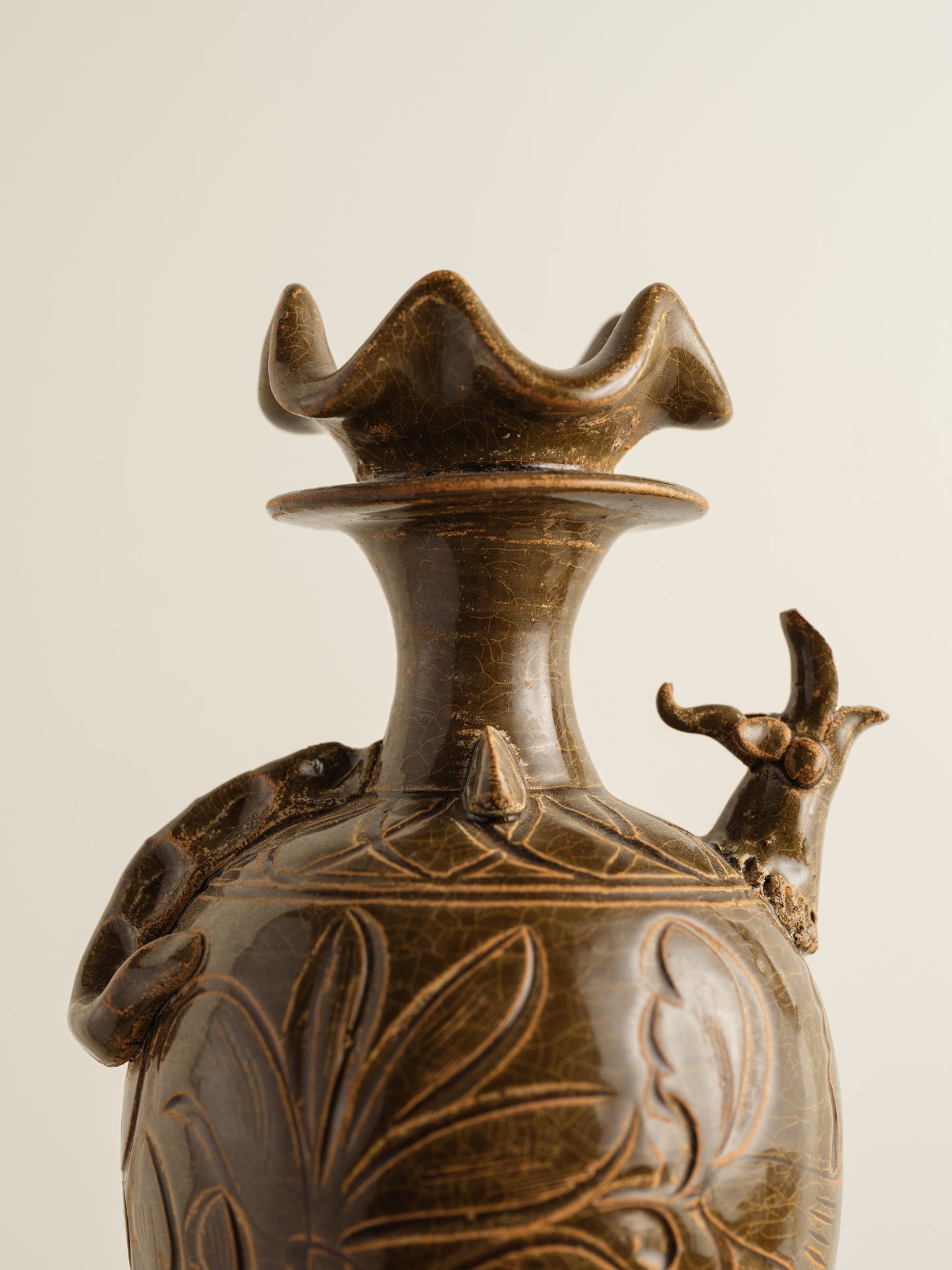 Brown stoneware ewer with carved lotus motif and flared crown-shaped mouth.