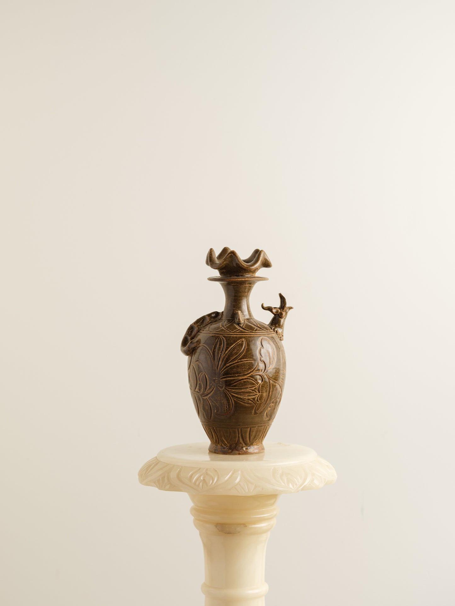 Brown stoneware ewer with carved lotus motif and flared crown-shaped mouth.