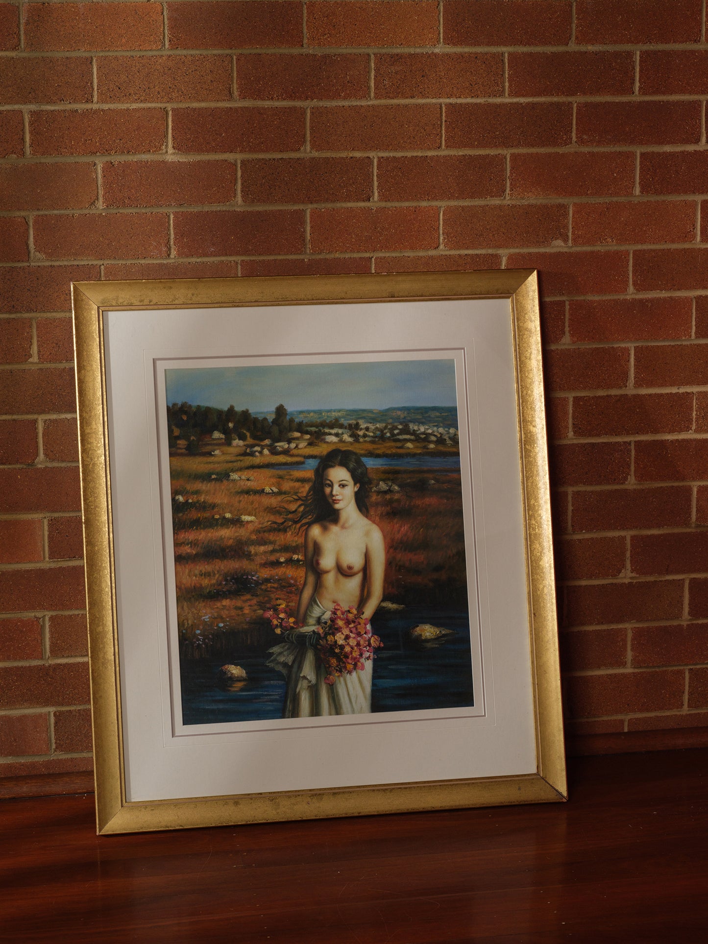 Framed artwork titled “Maiden of the Meadow” featuring a woman holding flowers in a meadow landscape, with gold frame and white mat.