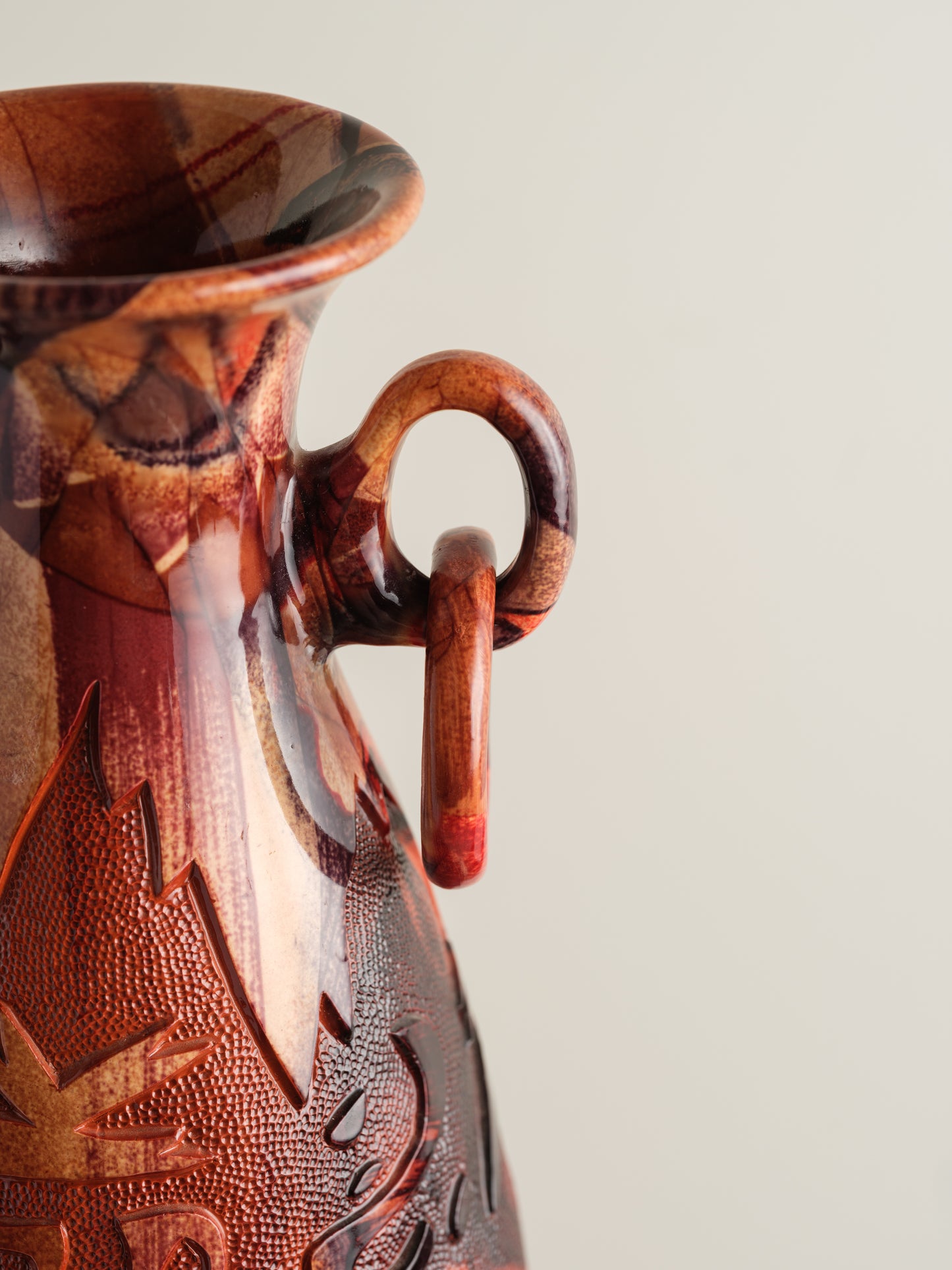 Decorative ceramic vase with red ochre glaze, featuring intricate carved motifs and twin ring handles.