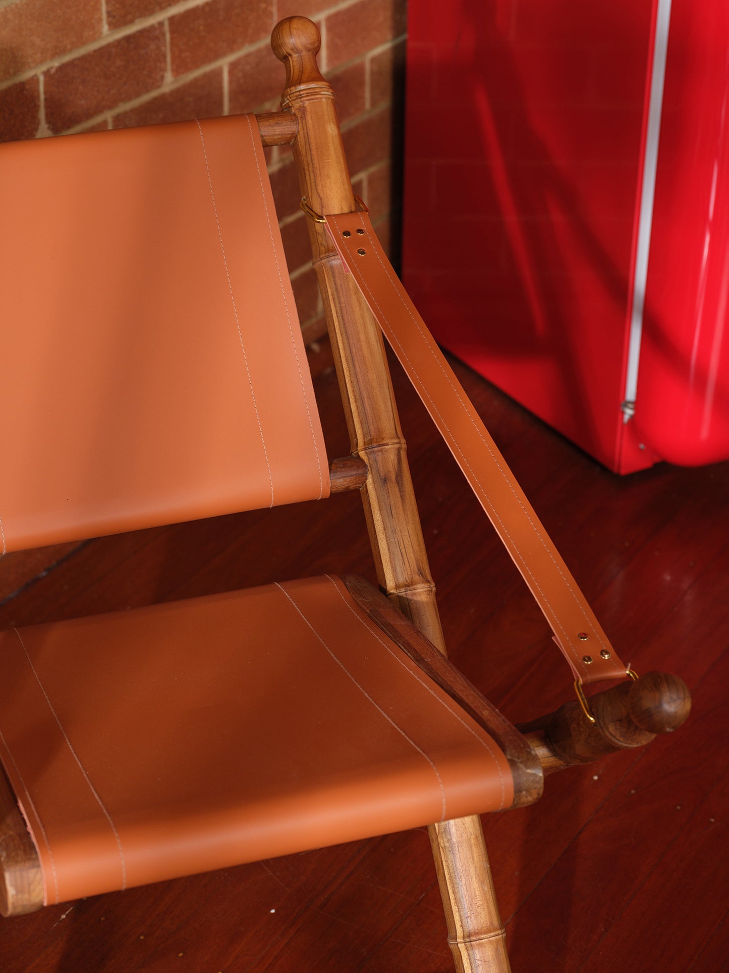 Replica faux bamboo and cognac leather safari style folding chair, vintage-inspired design, with brick wall