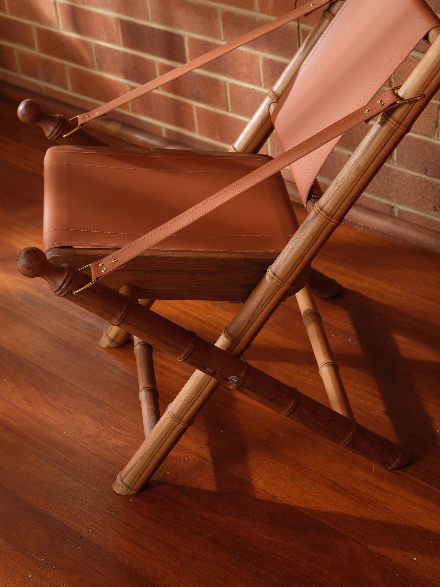 Replica faux bamboo and cognac leather safari style folding chair, vintage-inspired design, with brick wall