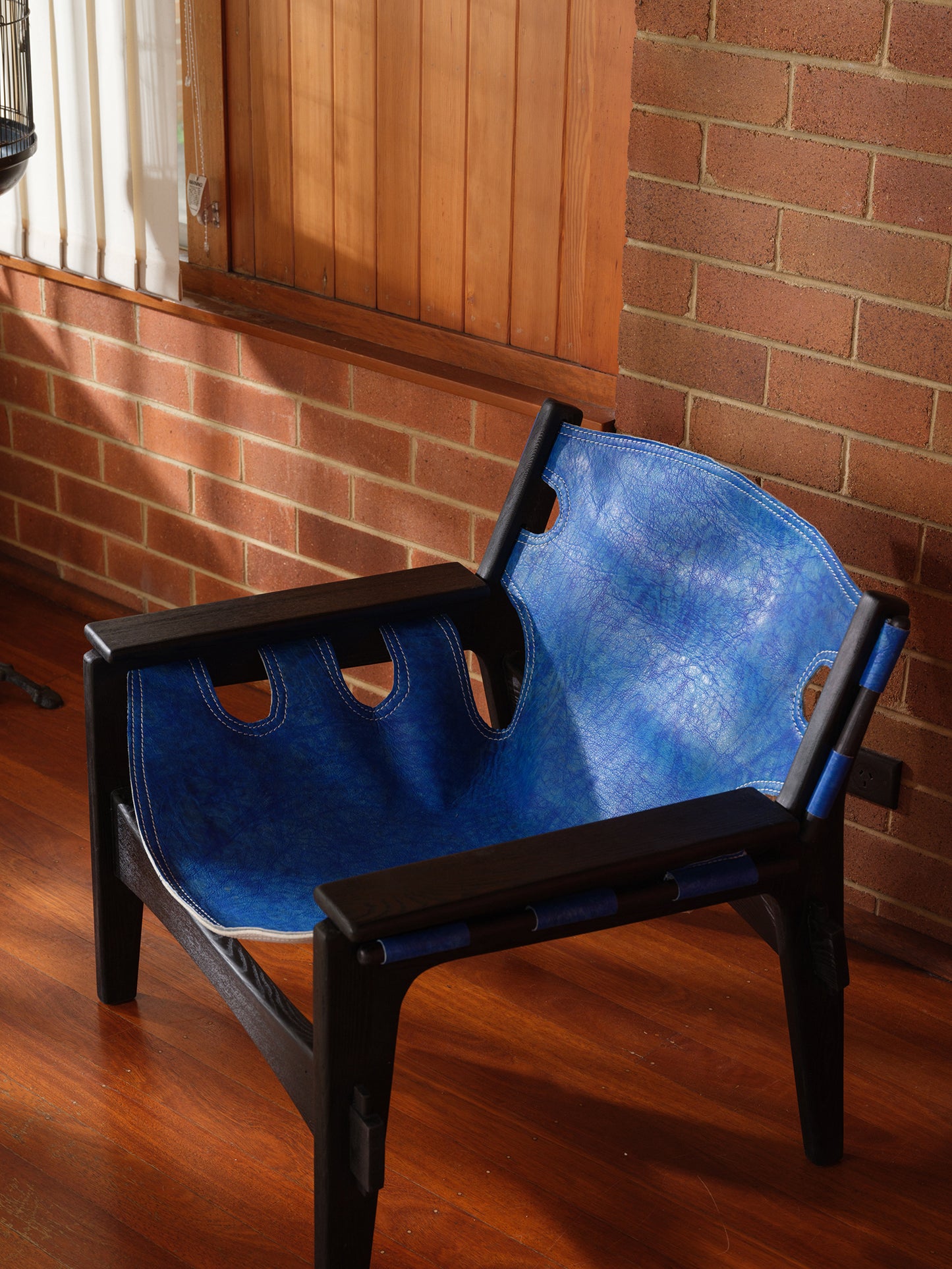 Replica Sergio Rodrigues Kilin lounge chair in blue leather with black wooden frame with brick wall