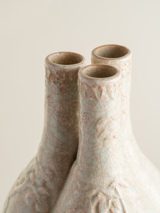 Celadon vase with three joined necks, embossed floral and bamboo motifs, and pale jade crackle glaze with russet tones.