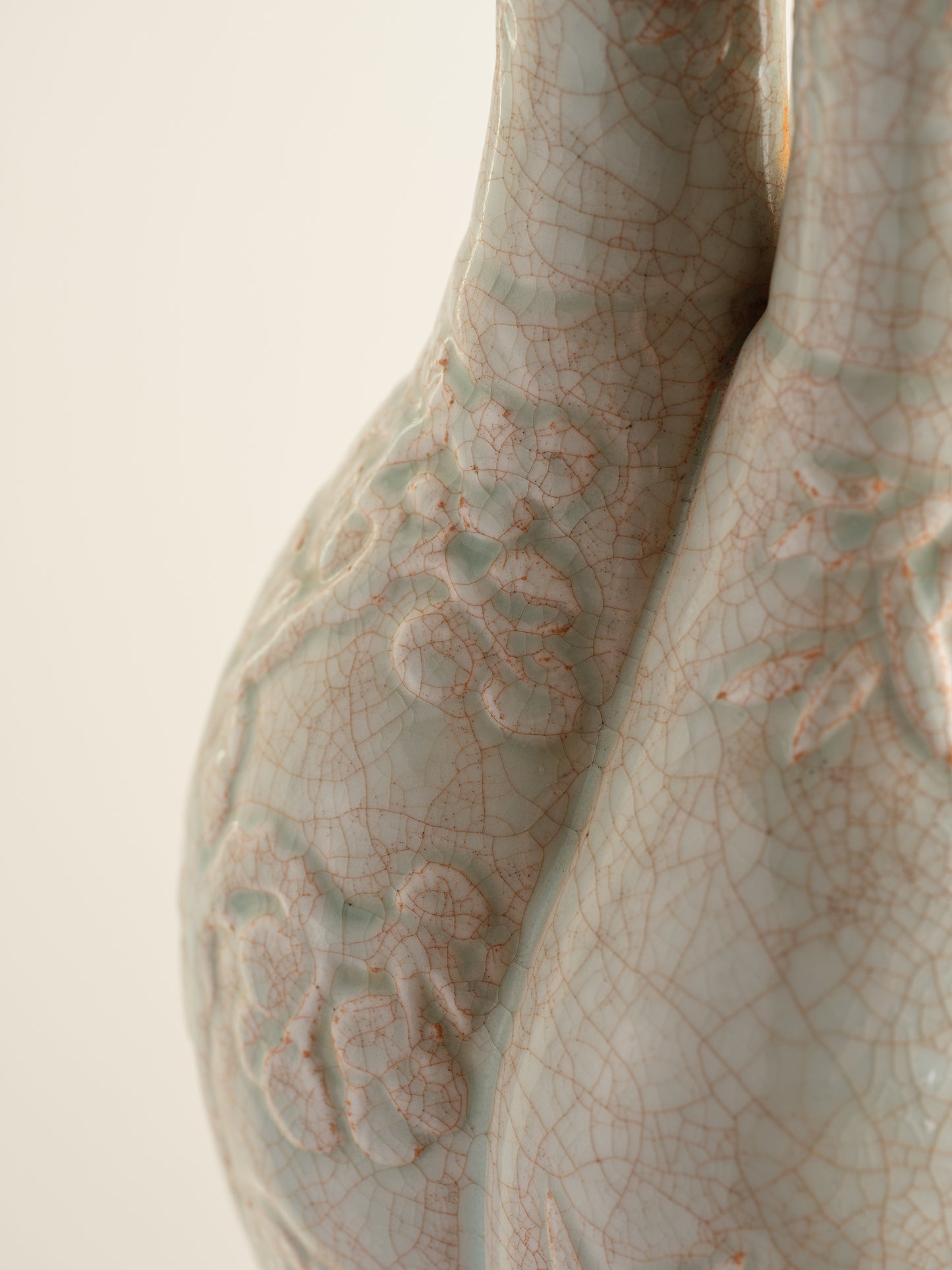 Celadon vase with three joined necks, embossed floral and bamboo motifs, and pale jade crackle glaze with russet tones.