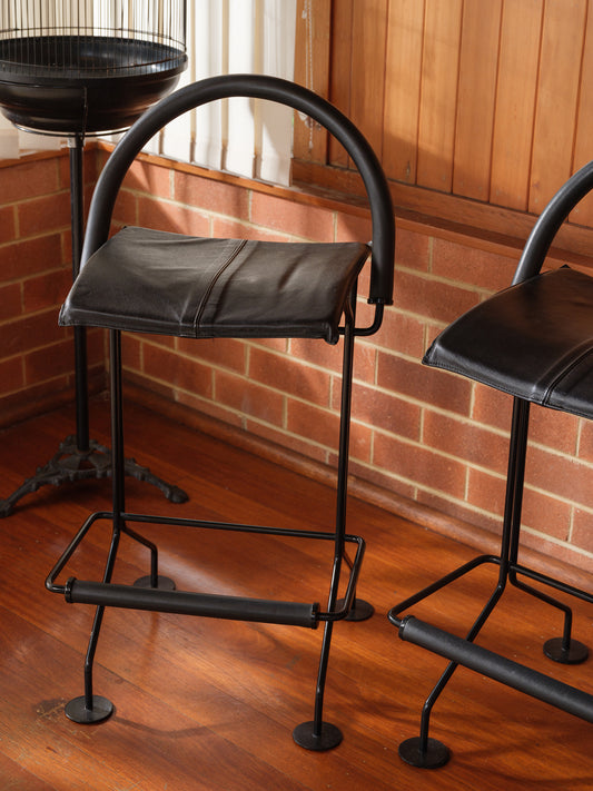 Vintage modern metal barstool with black leather seat and curved backrest.