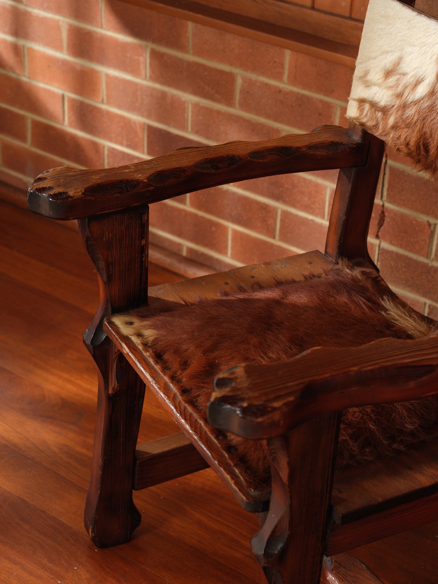 Wooden chair with a fur cushion against a brick wall.