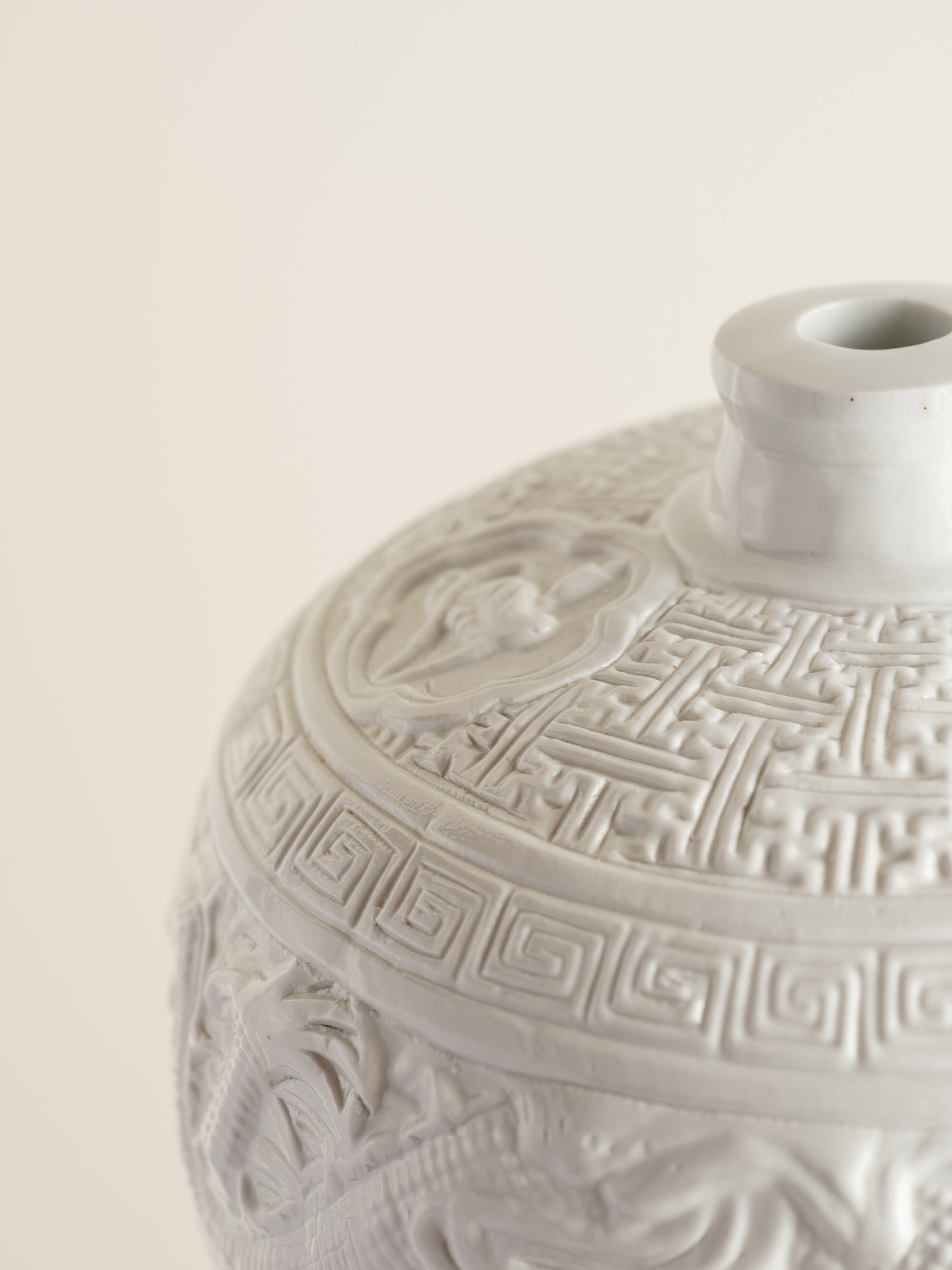 White porcelain meiping vase featuring intricate dragon relief motifs and geometric borders.