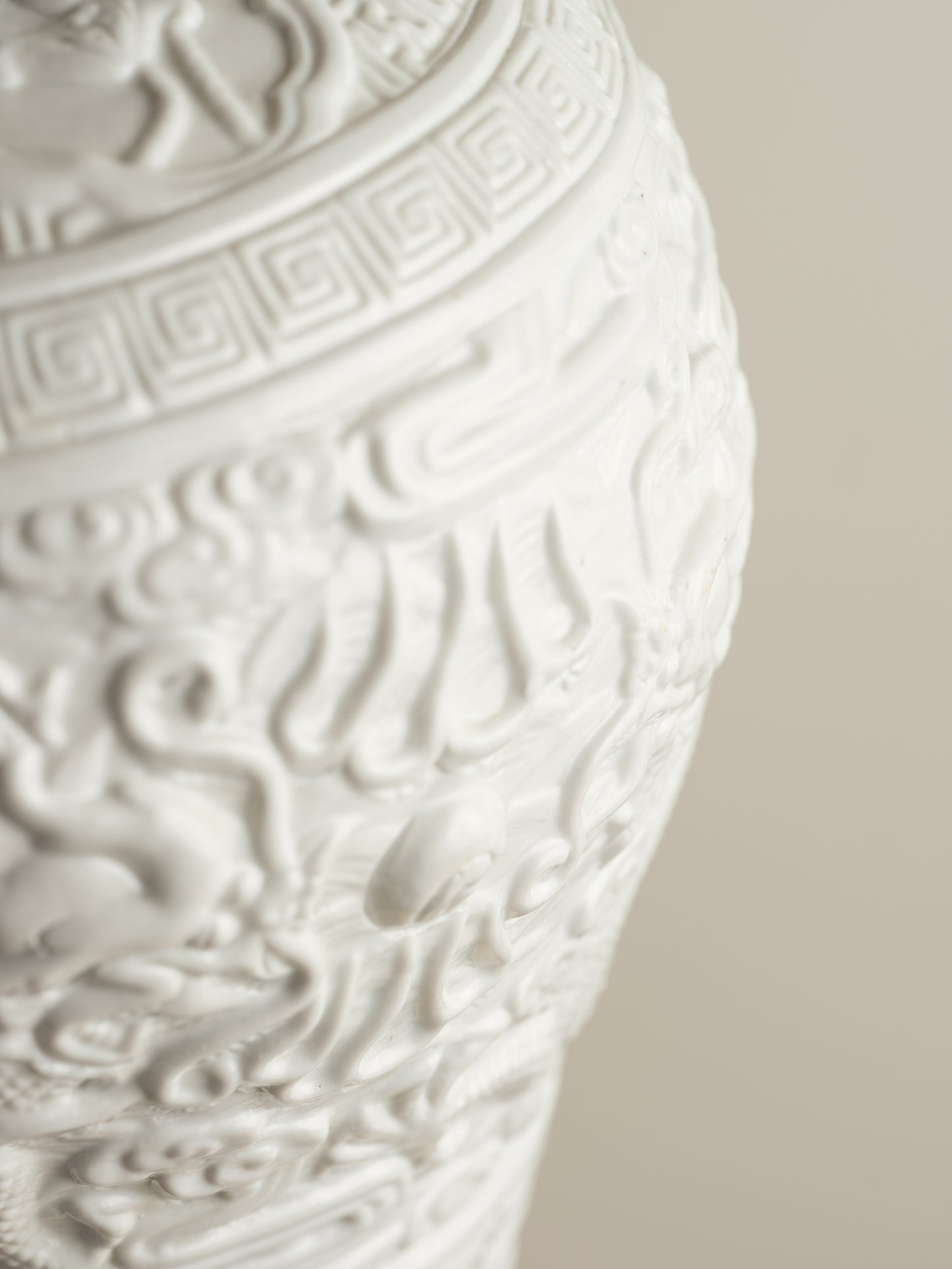 White porcelain meiping vase featuring intricate dragon relief motifs and geometric borders.