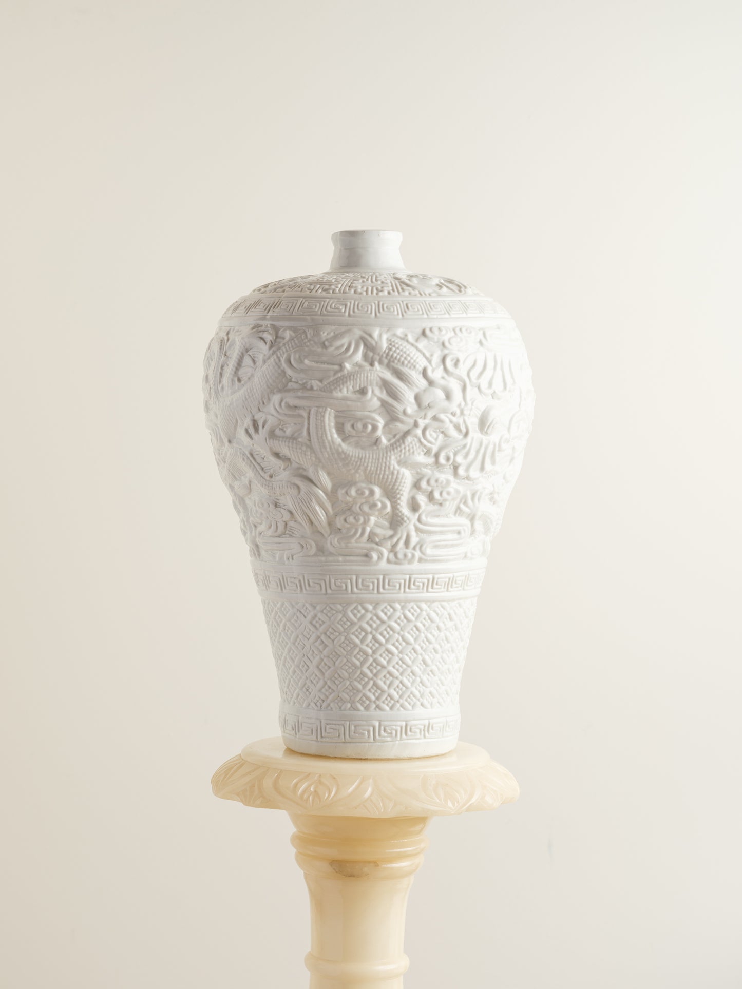 White porcelain meiping vase featuring intricate dragon relief motifs and geometric borders.