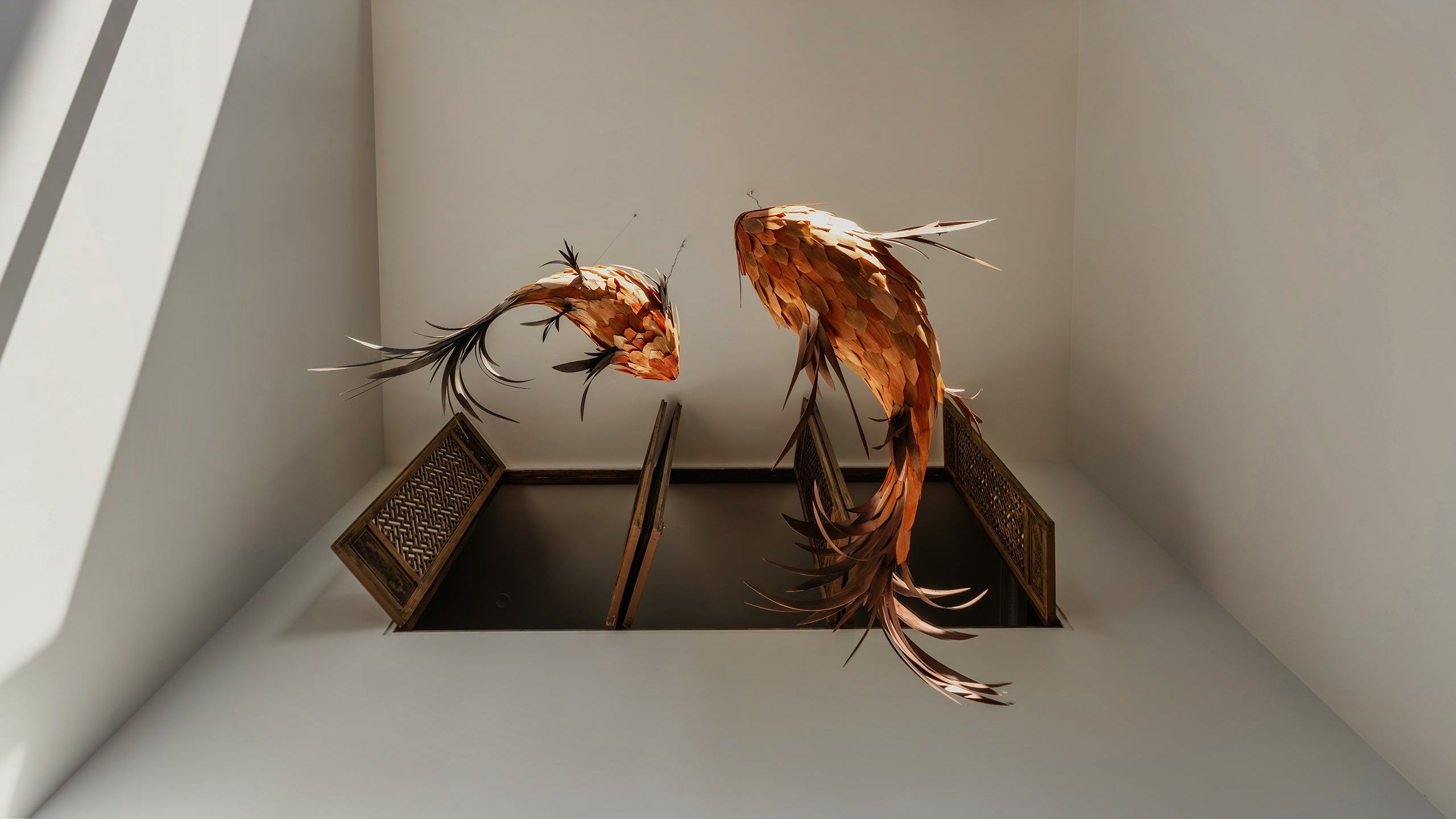 Wooden fish sculptures hanging from ceiling in modern atrium interior with glass skylight and decorative panels