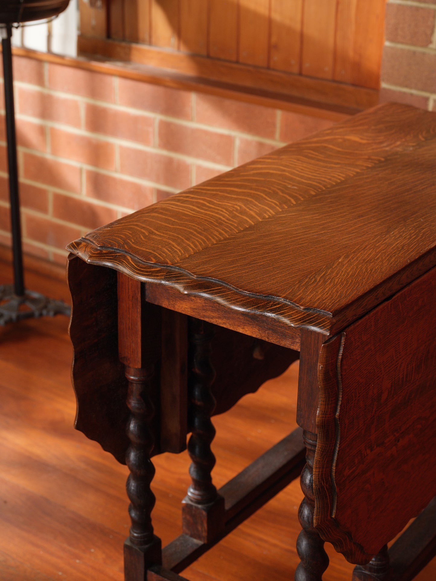Antique oak gateleg dining table with barley twist legs, drop-leaf design against brick wall background