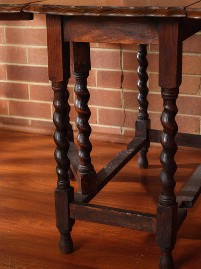 Antique oak gateleg dining table with barley twist legs, drop-leaf design against brick wall background