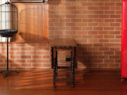 Antique oak gateleg dining table with barley twist legs, drop-leaf design against brick wall background