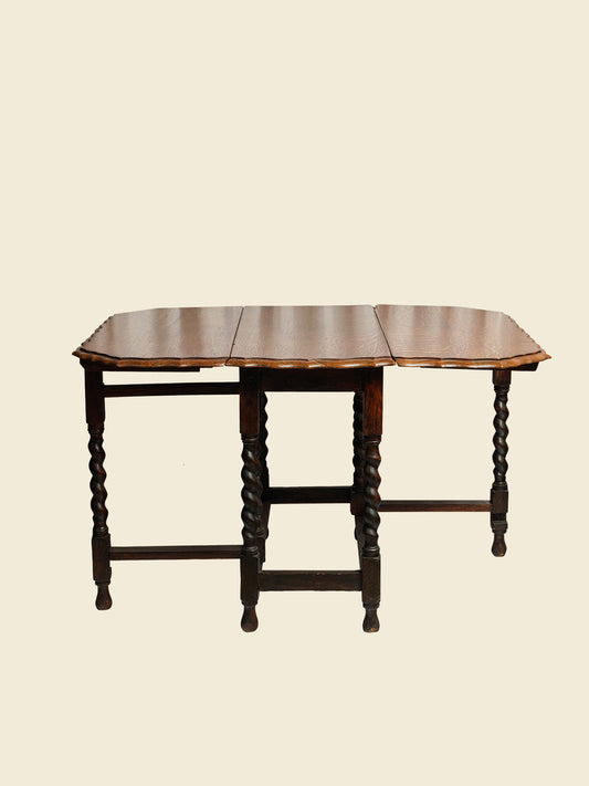 Antique oak gateleg dining table with barley twist legs, drop-leaf design against light wall background