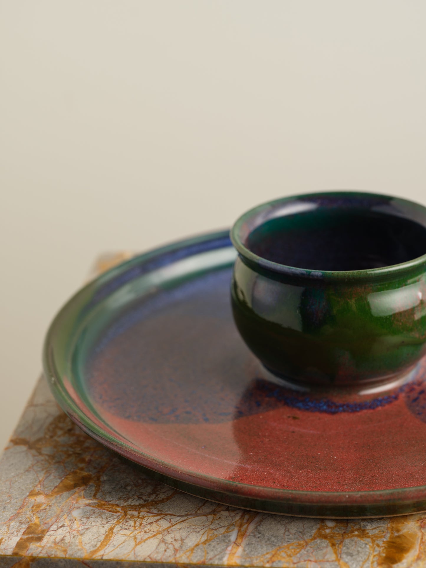 Hand-glazed ceramic bowl with matching charger in deep green and violet iridescent tones.