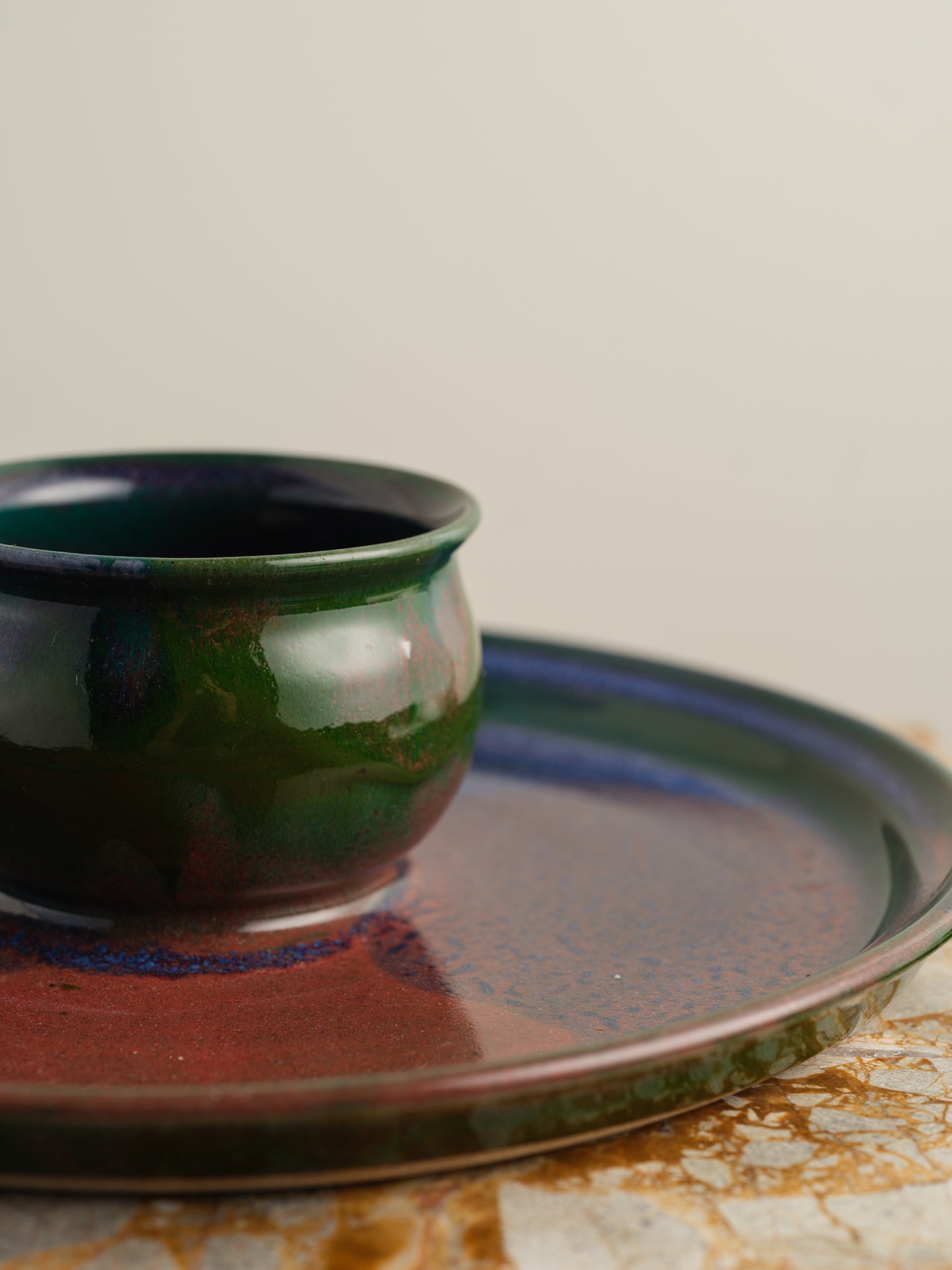 Hand-glazed ceramic bowl with matching charger in deep green and violet iridescent tones.