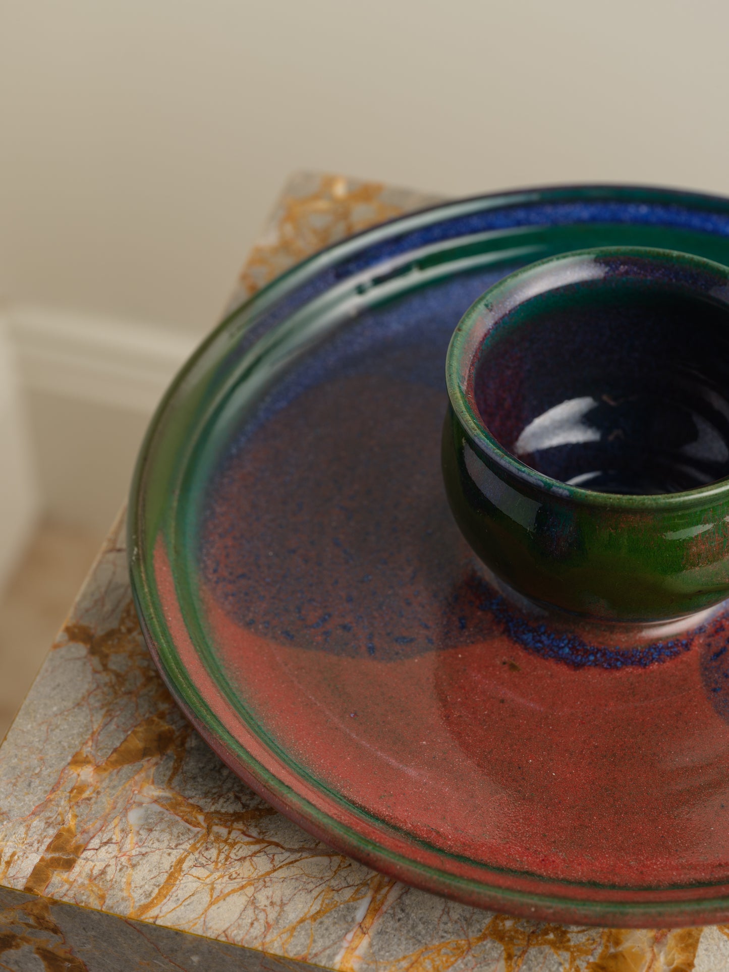 Hand-glazed ceramic bowl with matching charger in deep green and violet iridescent tones.