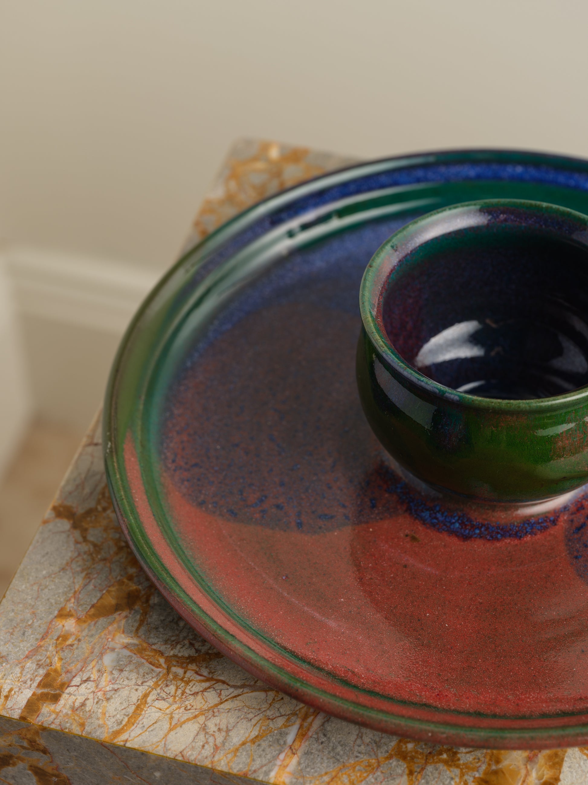 Hand-glazed ceramic bowl with matching charger in deep green and violet iridescent tones.