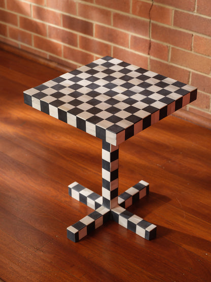 Modern black and white checkerboard side table with square top and pedestal base with brick wall background