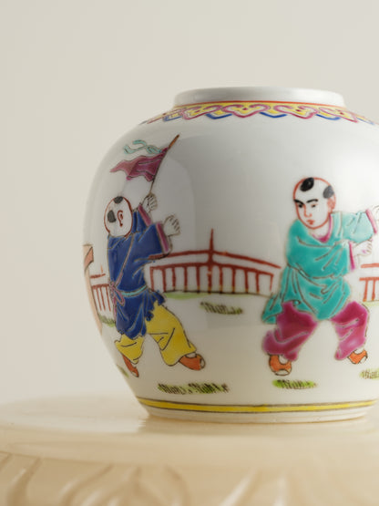 Small porcelain jar hand-painted with playful courtyard children in bright traditional robes.